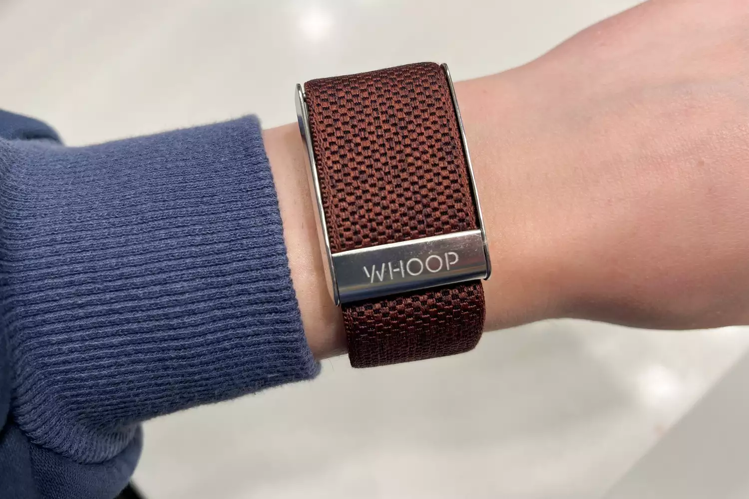 Close-up of a person's wrist wearing a Whoop 4.0 with a brown woven strap.