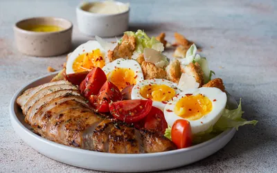 A healthy meal plate with grilled chicken, hard-boiled eggs, and fresh salad.