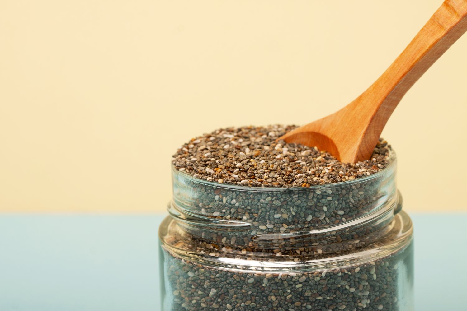 A glass jar of chia seeds on a bright yellow and blue background, symbolizing healthy dietary choices.