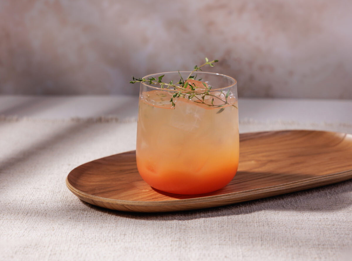 A close-up of a non-alcoholic grapefruit fizz with bubbles and fresh herb garnishes.