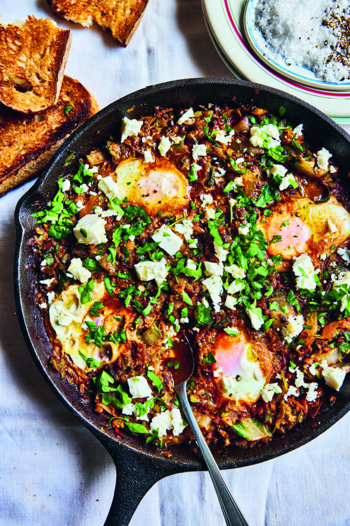 Green shakshuka in a skillet with lentils, leafy greens, and crumbled feta.