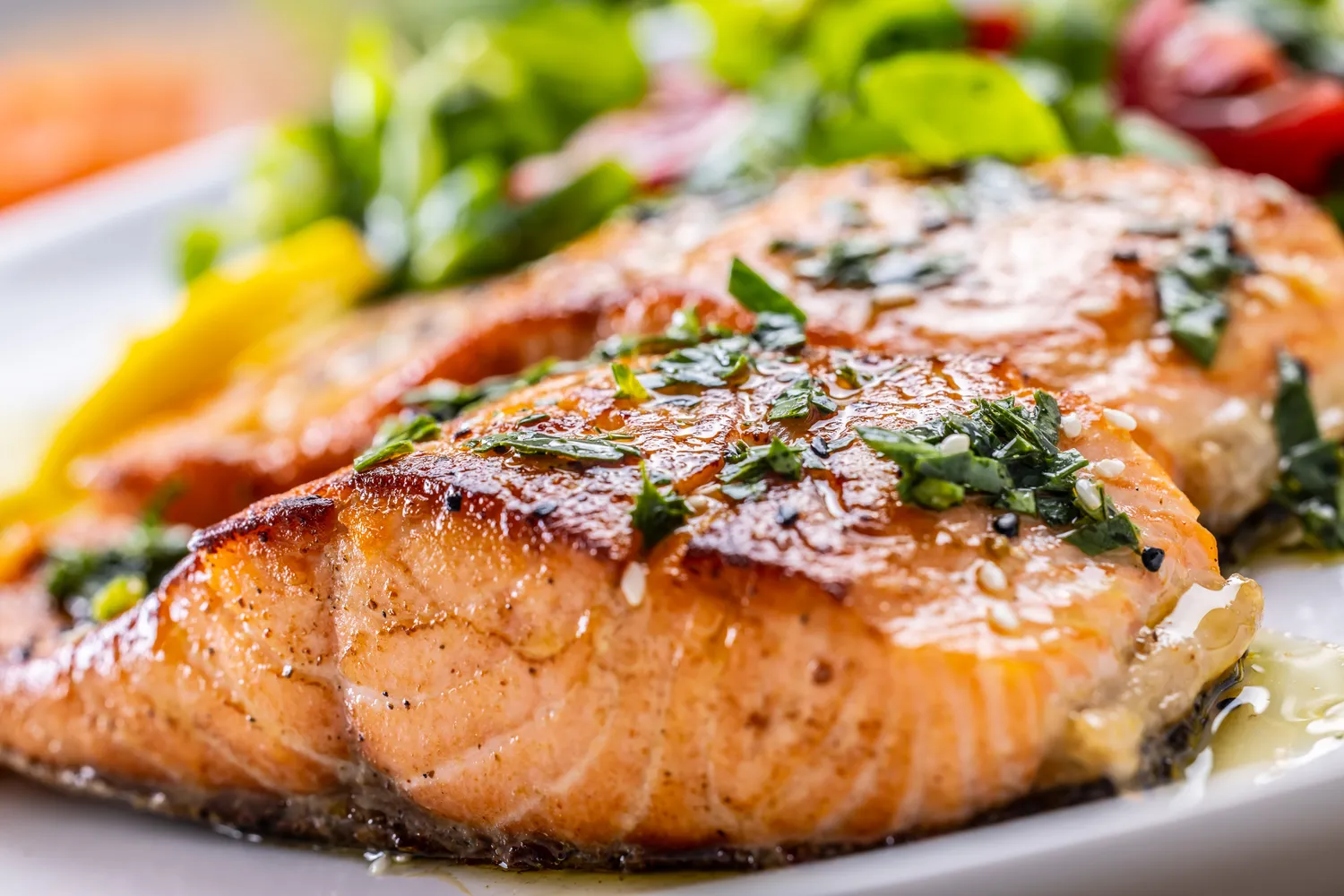 Seared salmon fillet garnished with herbs and sesame seeds on a white plate.