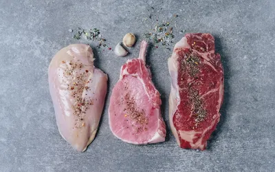 Various raw lean meats including chicken and beef seasoned with herbs.
