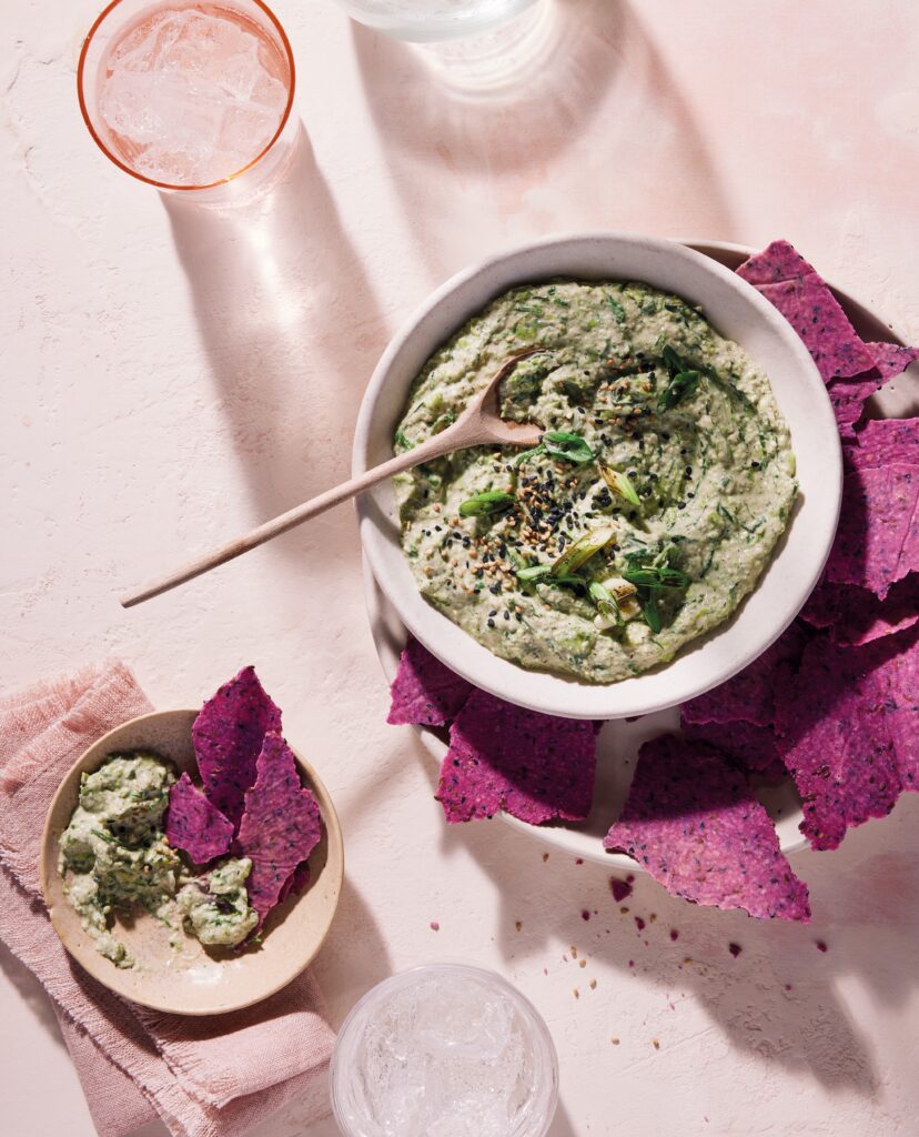 Close-up of a smooth green edamame spread topped with blackened, blistered spring onions in a stone bowl.