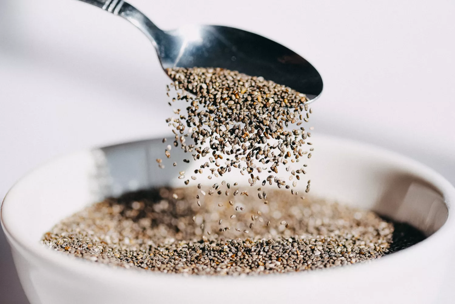 Close-up shot of chia seeds being poured into a white ceramic bowl.