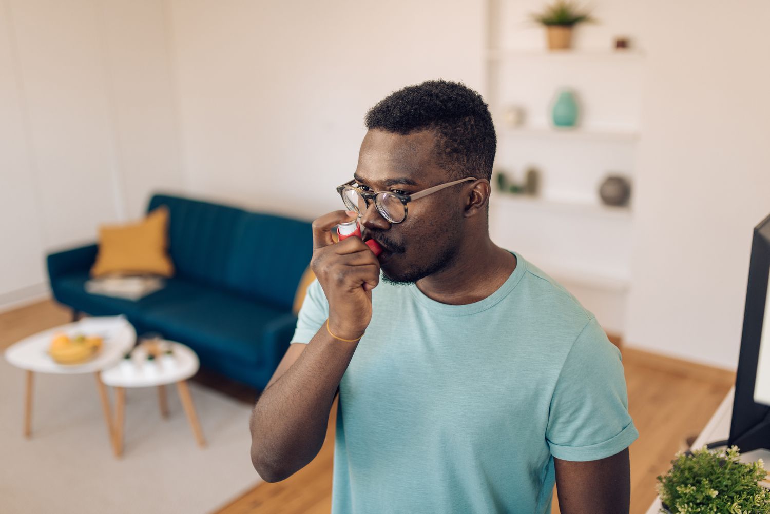 A man wearing glasses using an inhaler at home to manage a health condition.