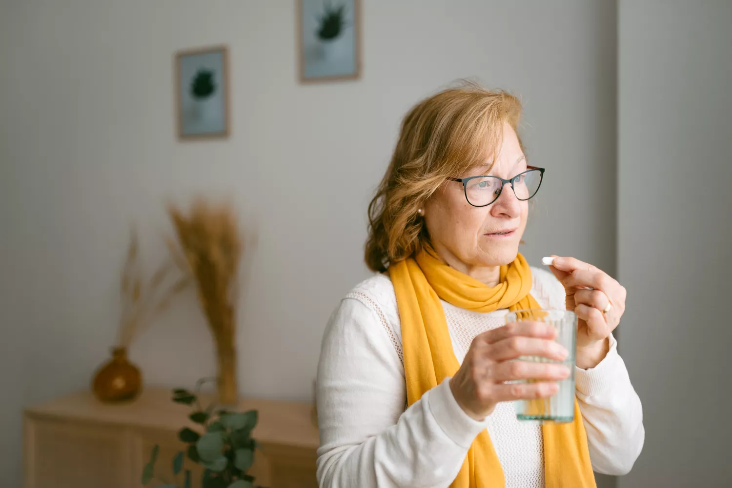 A person taking a supplement pill with a glass of water, illustrating proper intake.
