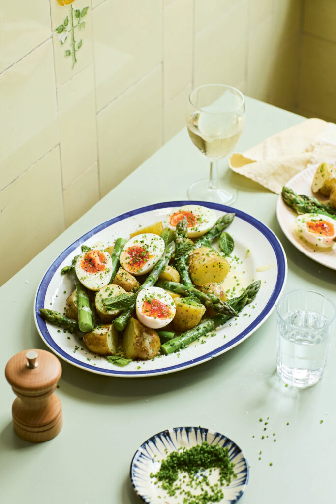 A golden-brown spring frittata with sliced new potatoes and asparagus tips served in a cast iron pan.