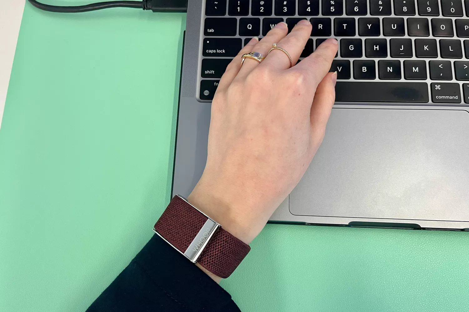 A person wearing a Whoop tracker while typing on a laptop.