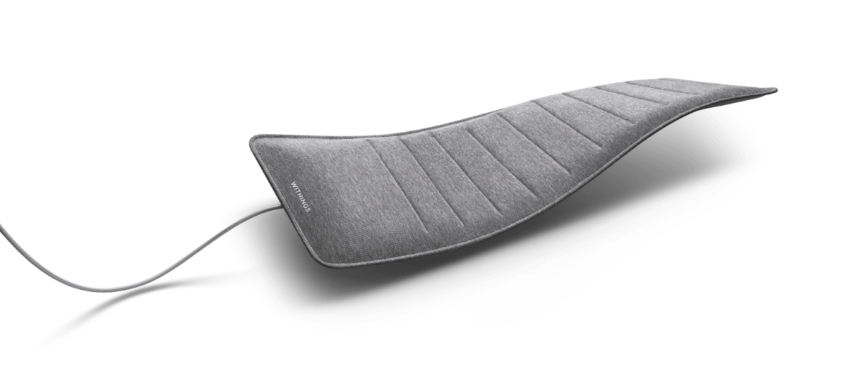 A person placing a slim, white Withings Sleep Analyzer sensor pad underneath a mattress.