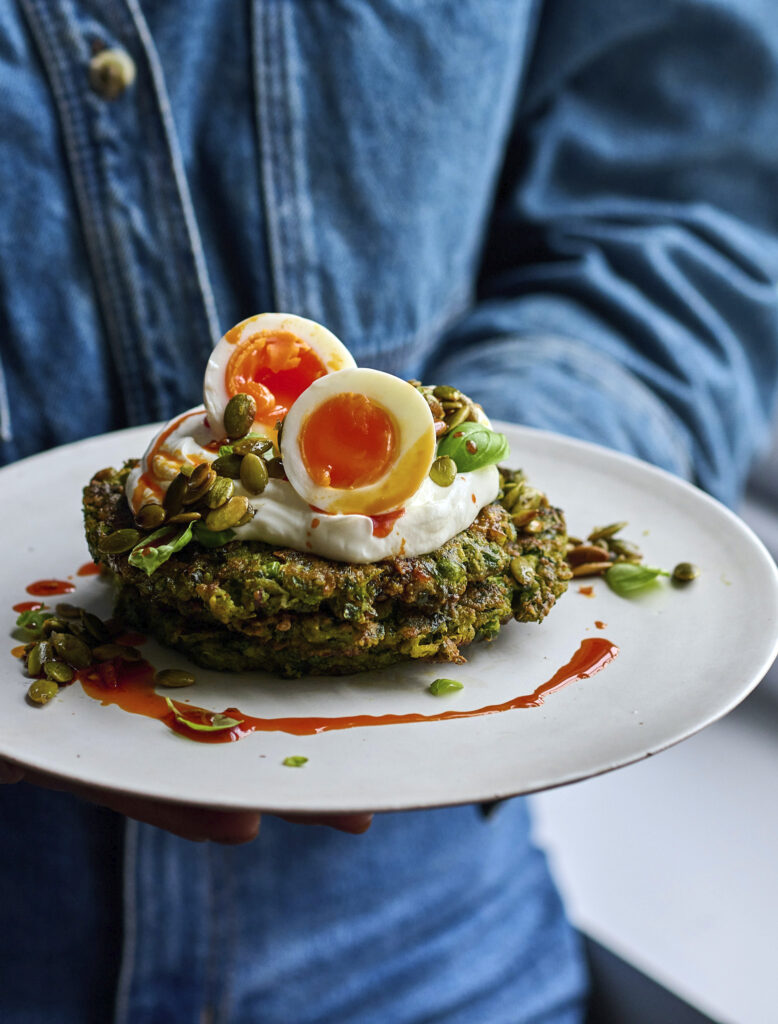 Herby pea pancakes served on a plate with yogurt, highlighting the golden-brown edges and green interior.