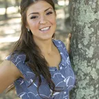 A smiling woman standing outdoors in a natural setting.