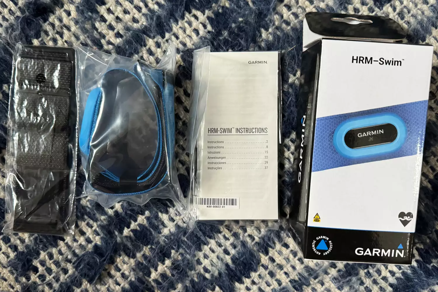 The Garmin HRM-Swim heart rate monitor unboxed with its blue non-slip strap and manual.