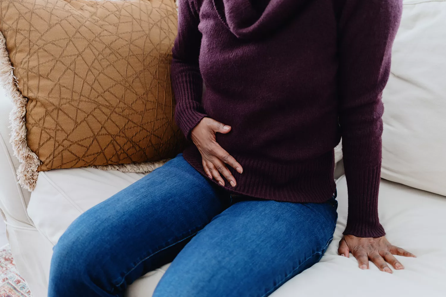A woman sitting on a couch holding her stomach in pain.