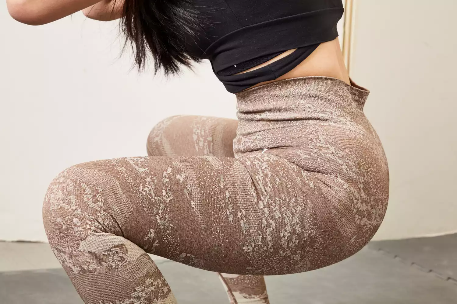A woman in camo-patterned leggings performing a deep squat in a minimalist gym.