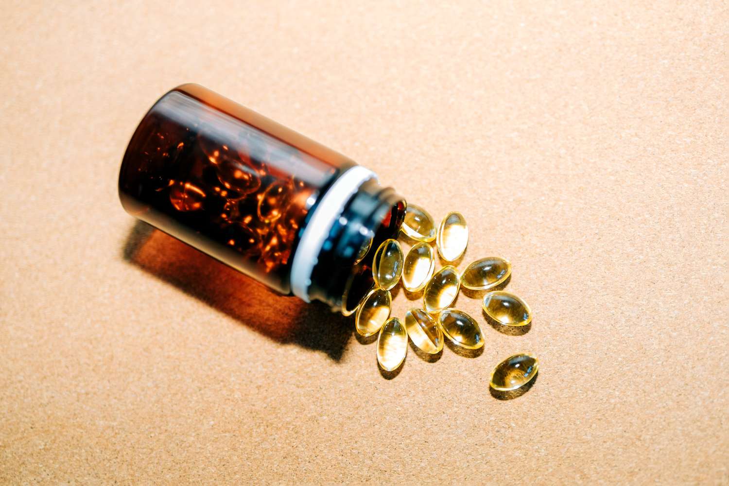 White Vitamin D supplement capsules spilling out of a brown glass bottle on a clean surface.
