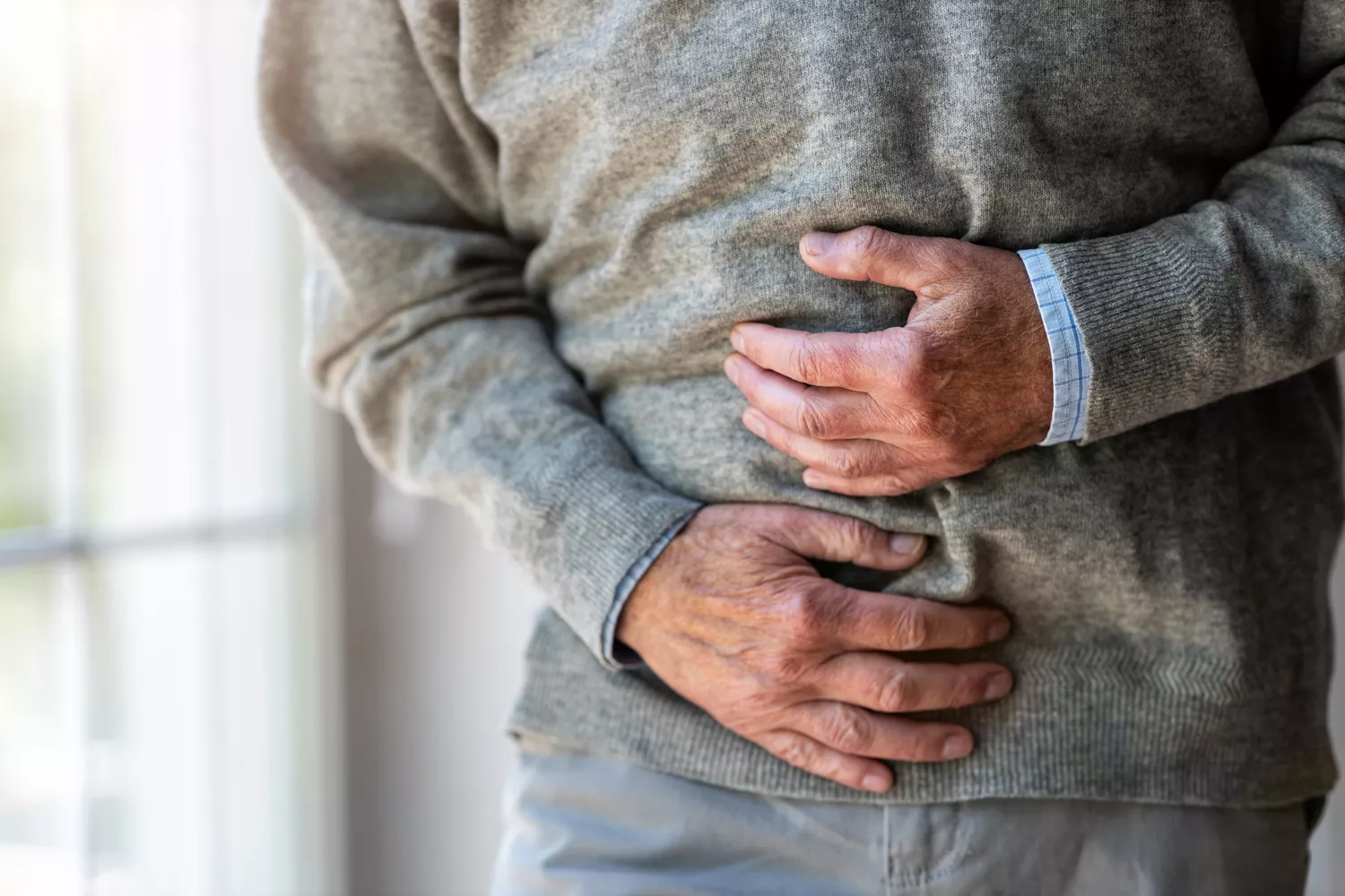 An older adult in a indoor setting holding their stomach, indicating abdominal pain.
