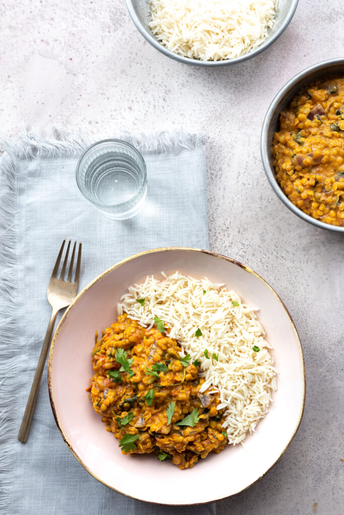 A close-up of golden-red lentil dahl swirled with coconut milk and topped with vibrant green watercress.