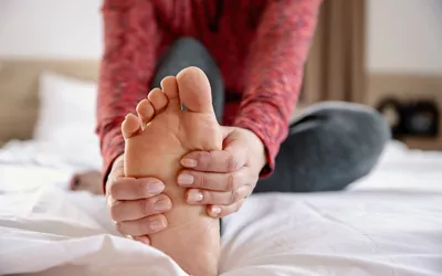 A person sitting on a bed and massaging their foot to relieve tension.