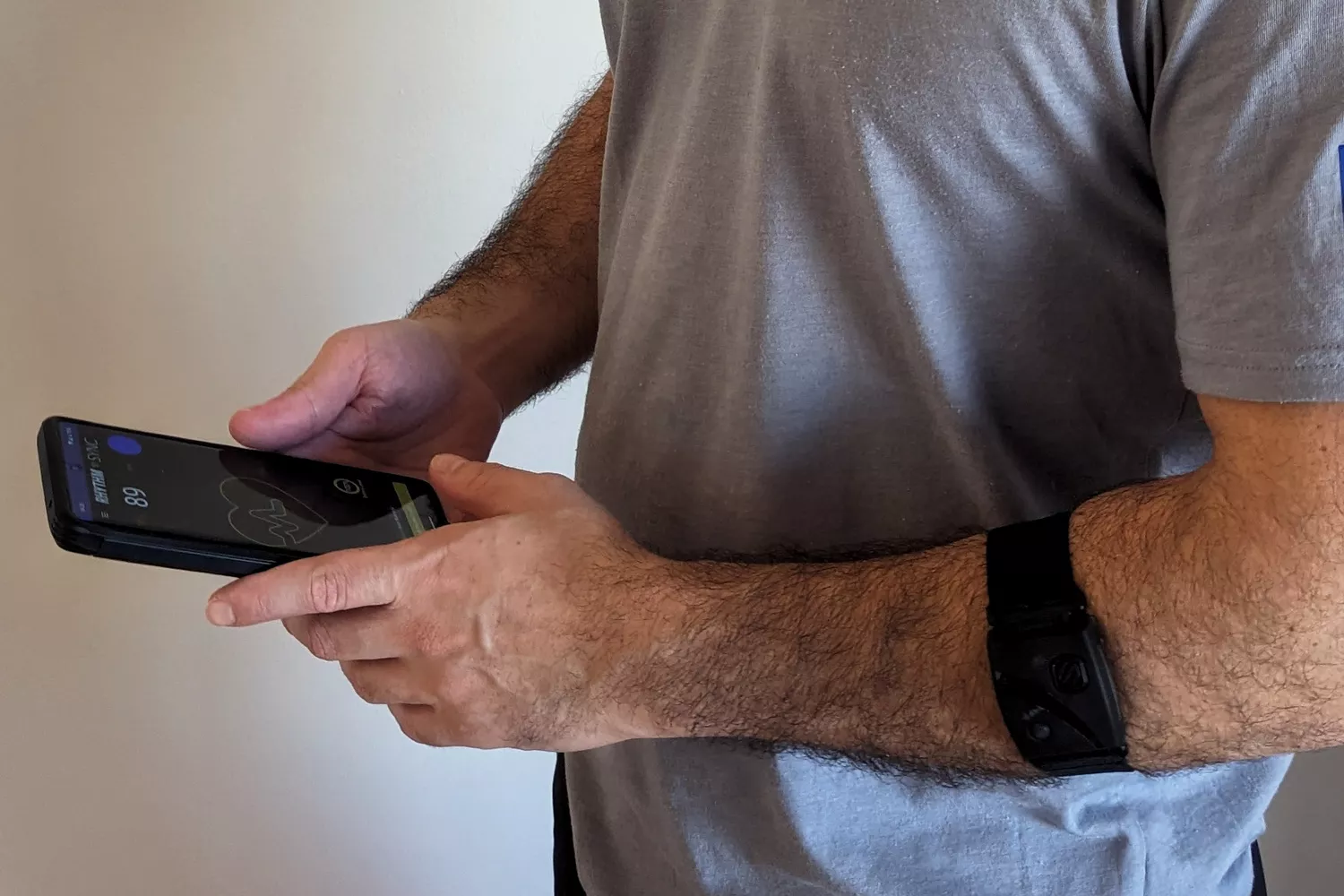 A person wearing a Scosche Rhythm24 armband while checking heart rate data and an ECG waveform on a smartphone.