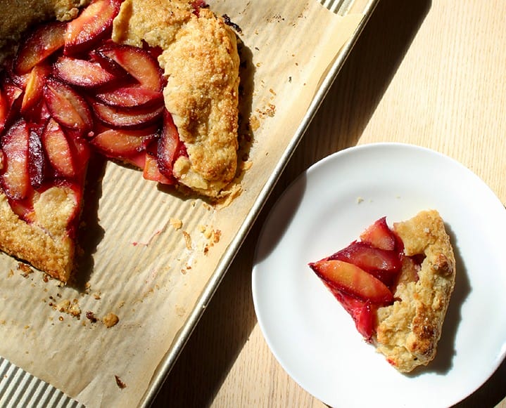 A slice of warm plum galette served on a plate with a melting scoop of vanilla bean ice cream.