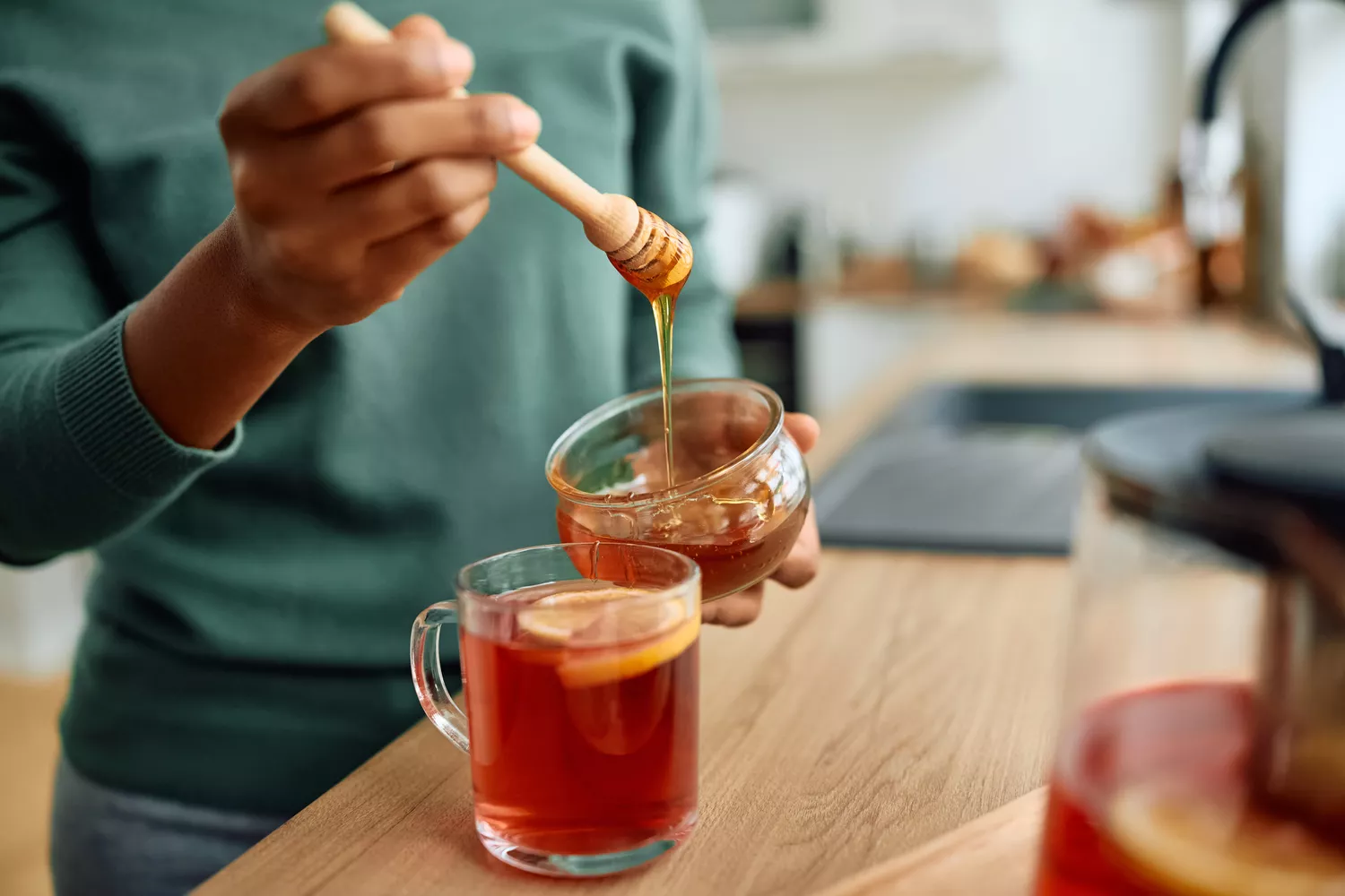 A woman adding honey to a cup of hot tea, representing a typical glucose-impacting food choice.