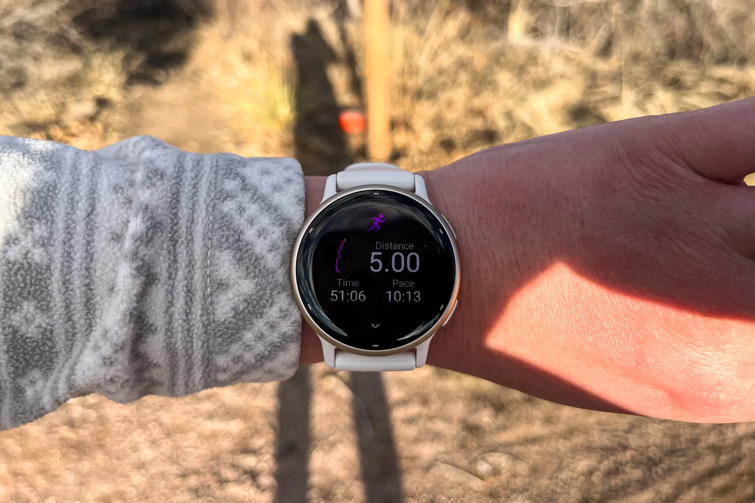 A white smartwatch displaying distance, time, and pace metrics during an outdoor run.