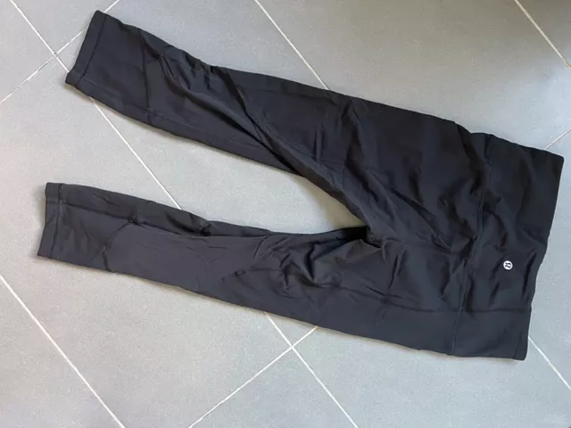 Black Lululemon high-rise leggings laid flat on a neutral tiled floor.
