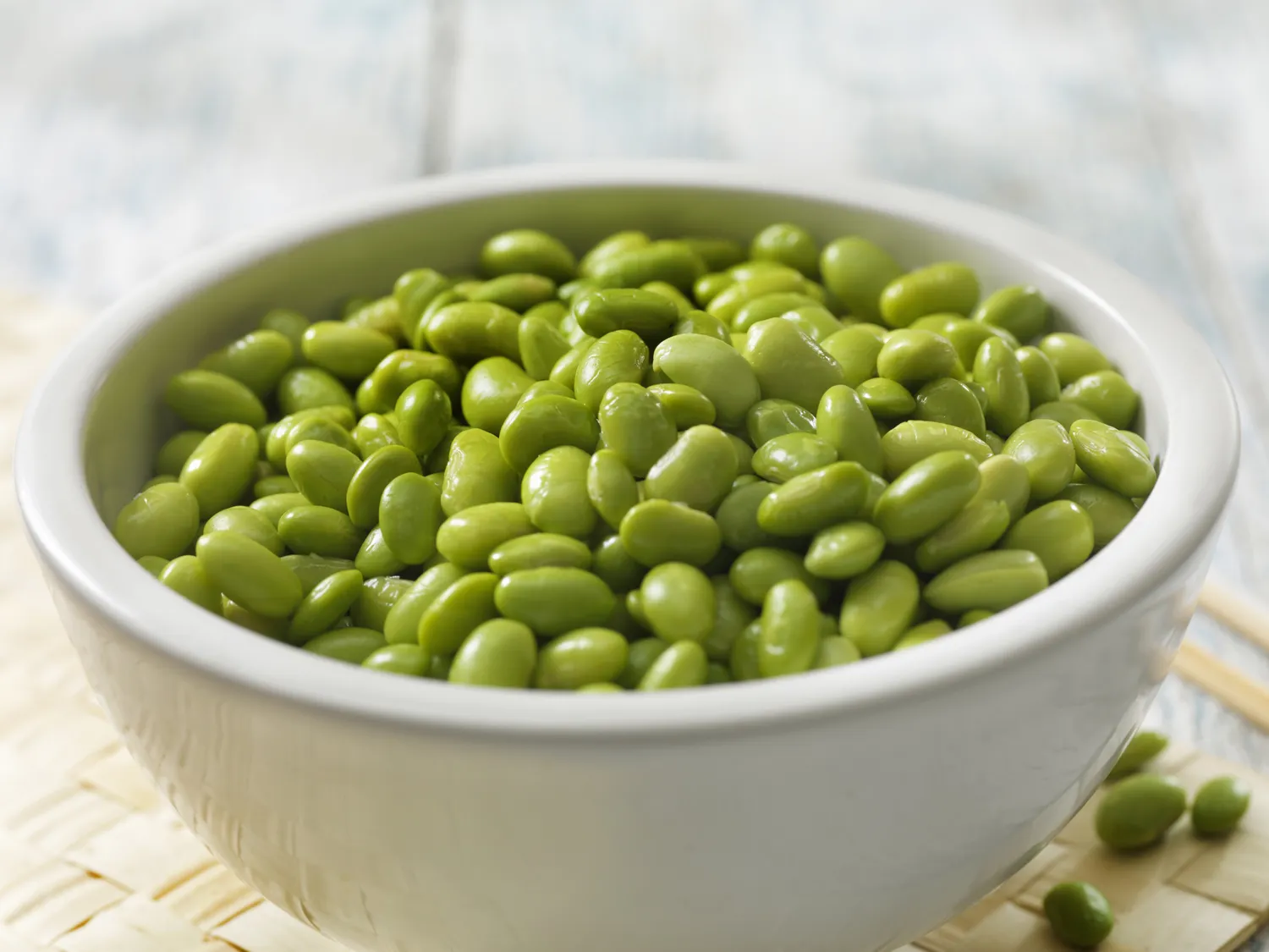 A white bowl filled with edamame beans on a light surface.