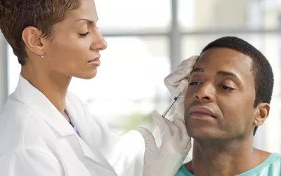 A healthcare professional in a white coat administering a forehead injection to a patient.