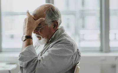 An elderly man holding his forehead in distress, suggesting a headache or emotional fatigue.