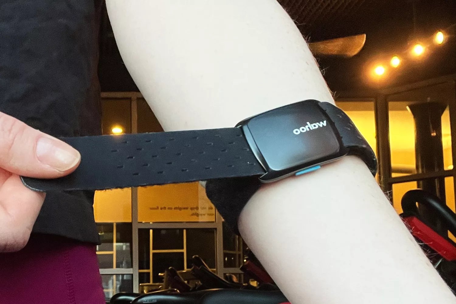 A person in a gym adjusting a Wahoo Tickr Fit heart rate monitor armband on their forearm.