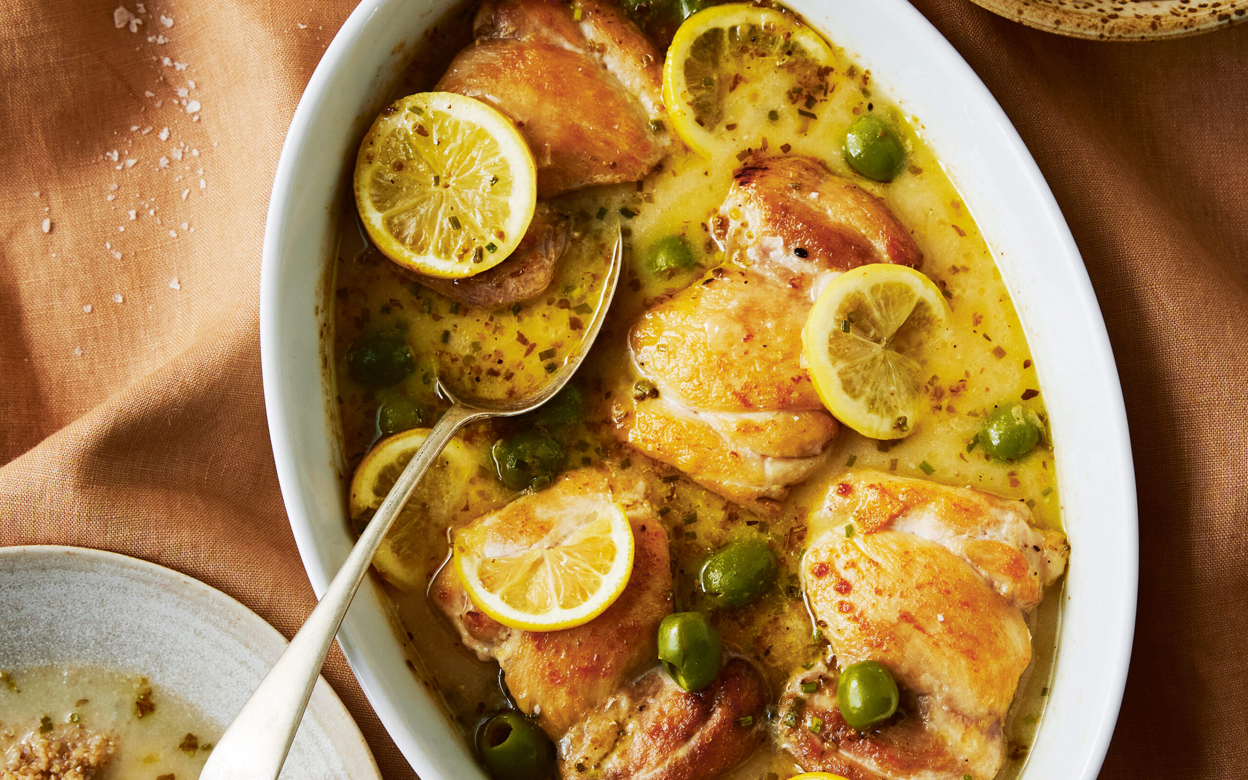 A close-up shot of a one-pan lemon chicken dish with herbs and olives.