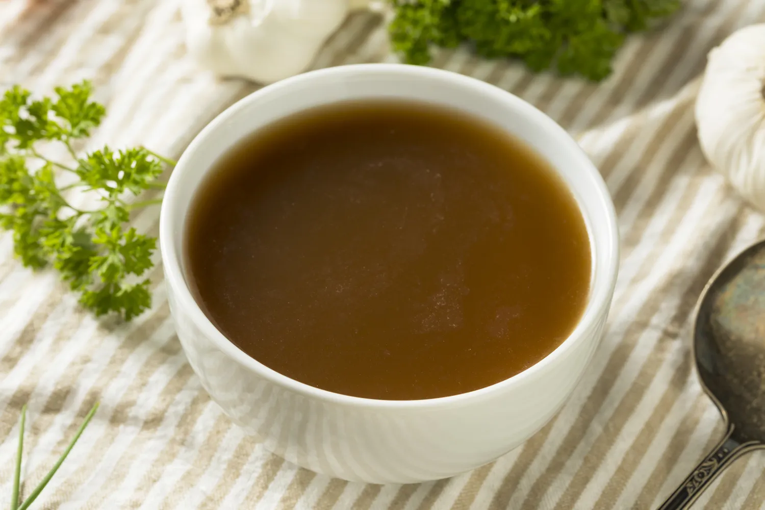 A bowl of rich brown broth with fresh parsley and garlic, suggesting a healing meal.