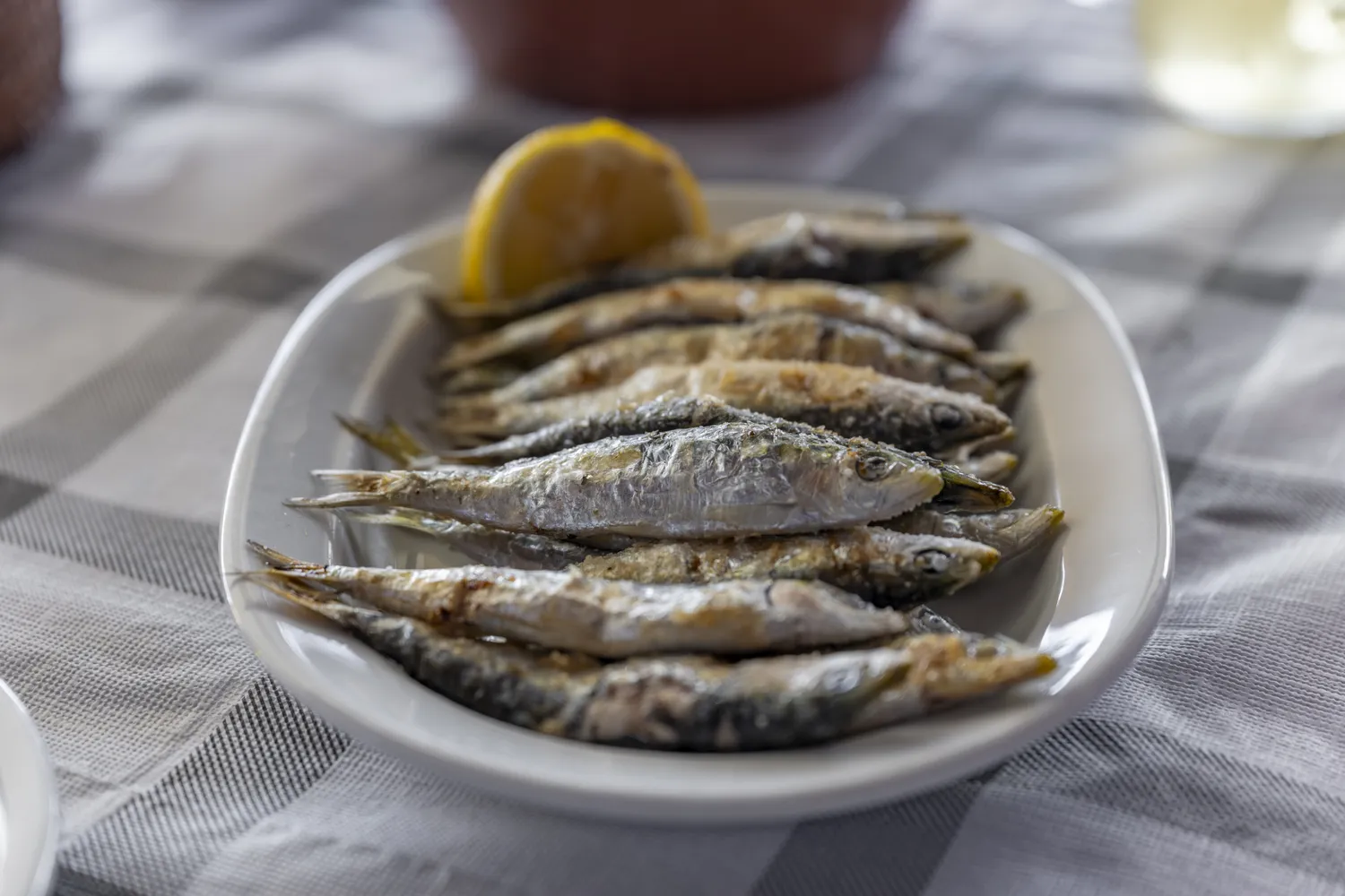 Grilled sardines with a lemon wedge on a checkered tablecloth.