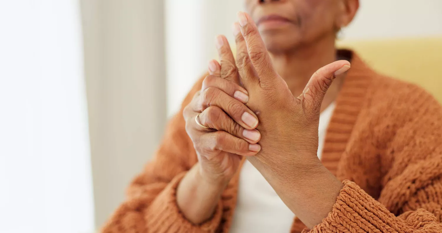 A woman in a sweater gently massaging her hand to alleviate muscle tightness.