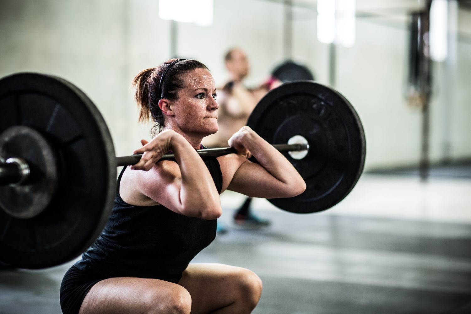 A female athlete performing a barbell back squat with focused form in a gym environment.
