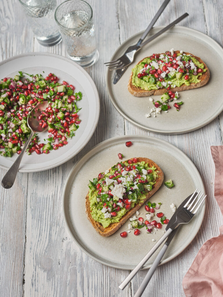 Close-up of pomegranate mint salsa layered over whipped goat cheese and avocado on toasted sourdough.