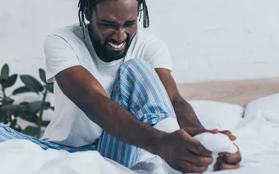 A man sitting on a bed holding his foot in pain, representing the initial recovery phase.