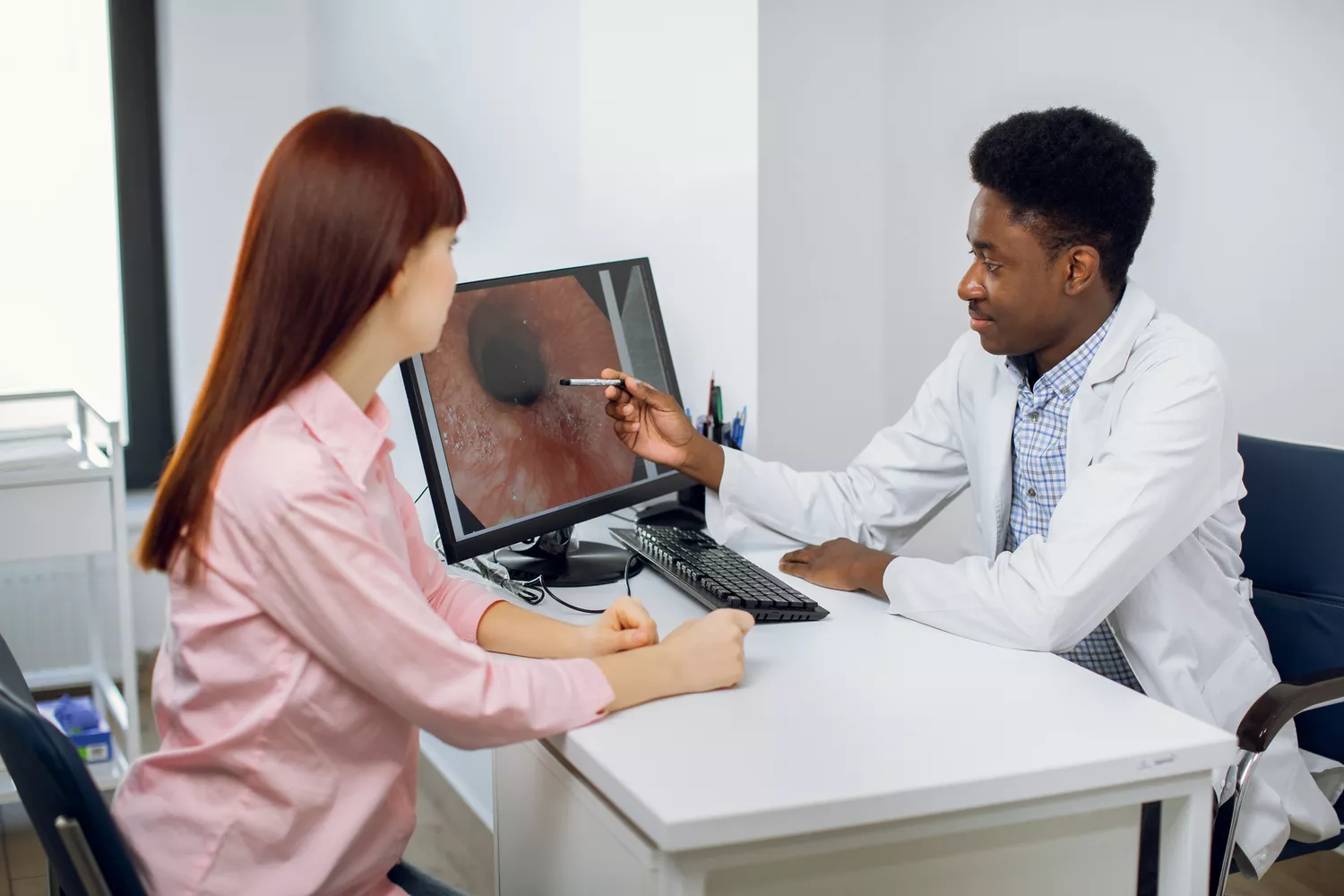A doctor in a white coat shows diagnostic images to a patient during a medical consultation.