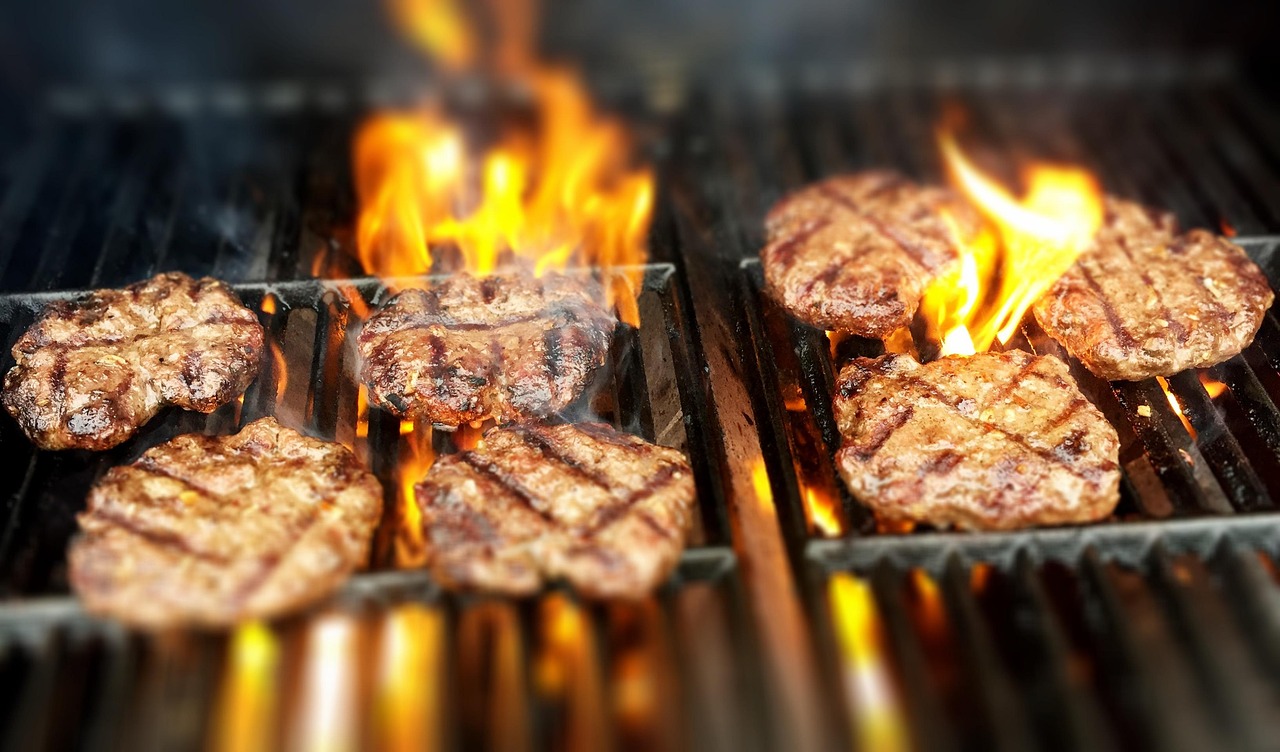 A plant-based burger patty being flipped on a hot outdoor grill with visible sear marks