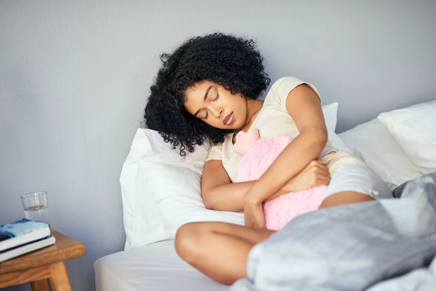 A woman lying in bed looking uncomfortable and holding her lower abdomen.