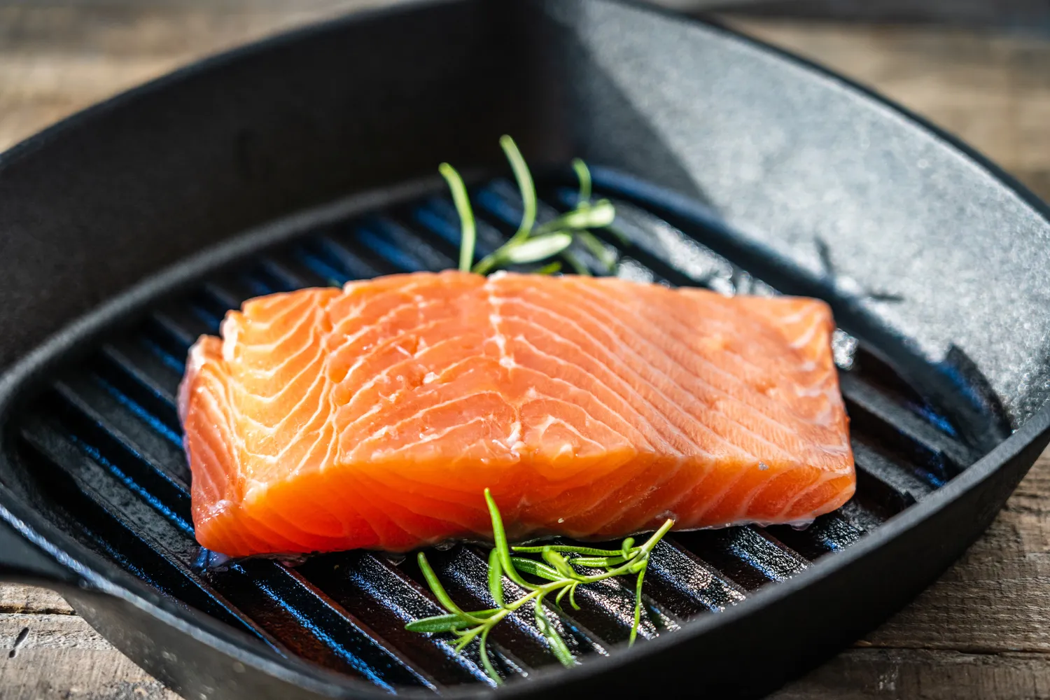 A fresh salmon fillet with rosemary sprigs in a grill pan, ready for healthy cooking.