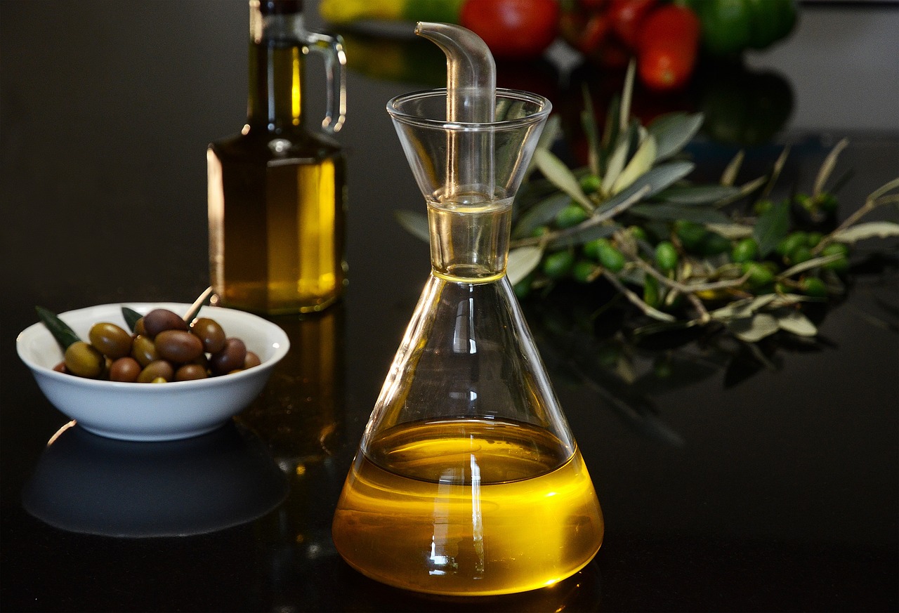 A glass bottle of golden olive oil next to fresh herbs