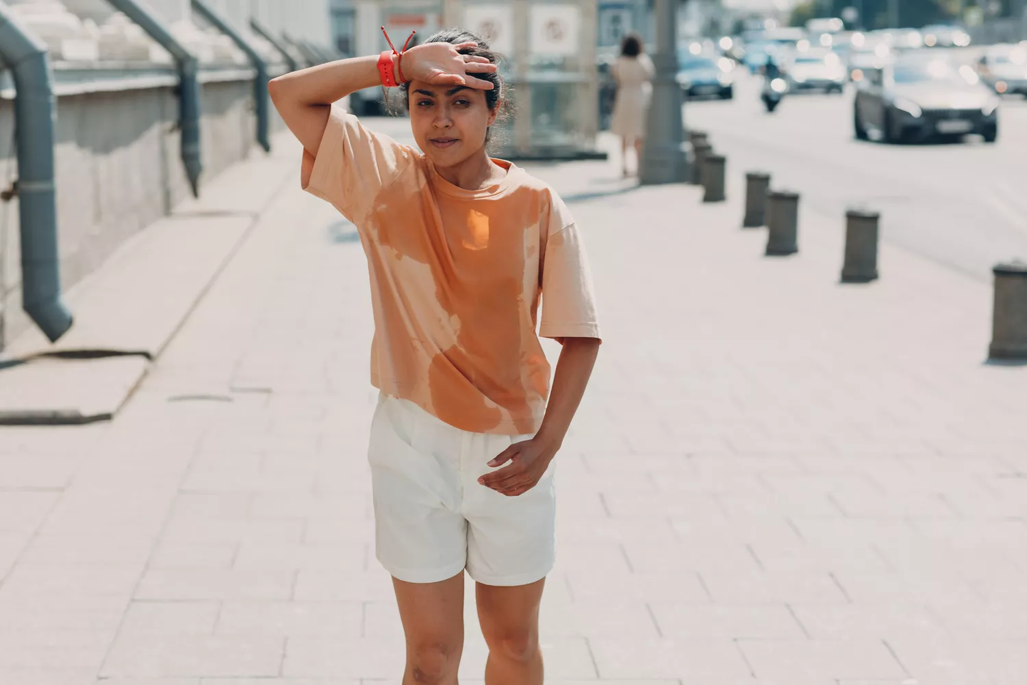 A person on a city street with a visible large wet sweat stain on their shirt.