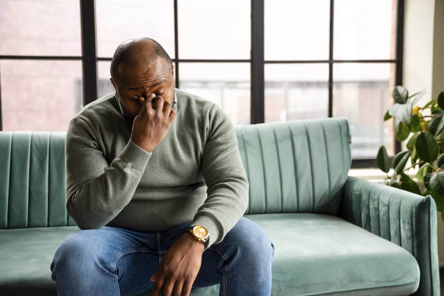 A man on a green sofa rubbing his eyes, showing signs of morning fatigue and stress.