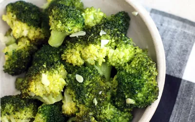 A bowl of steamed broccoli with garlic on a checkered cloth, representing healthy meal preparation for patients.