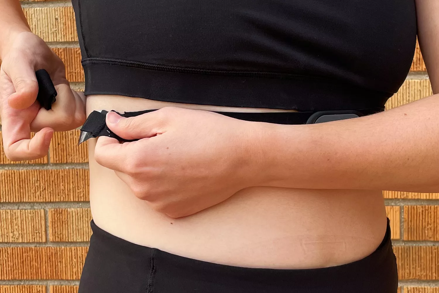 A person in athletic gear adjusting a black chest strap heart rate monitor around their torso.