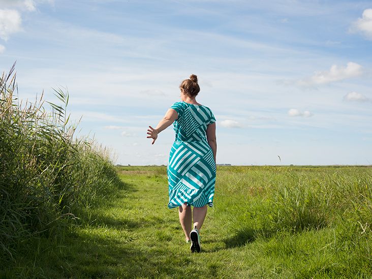 A woman in a patterned dress walking along a grassy path in a nature setting.
