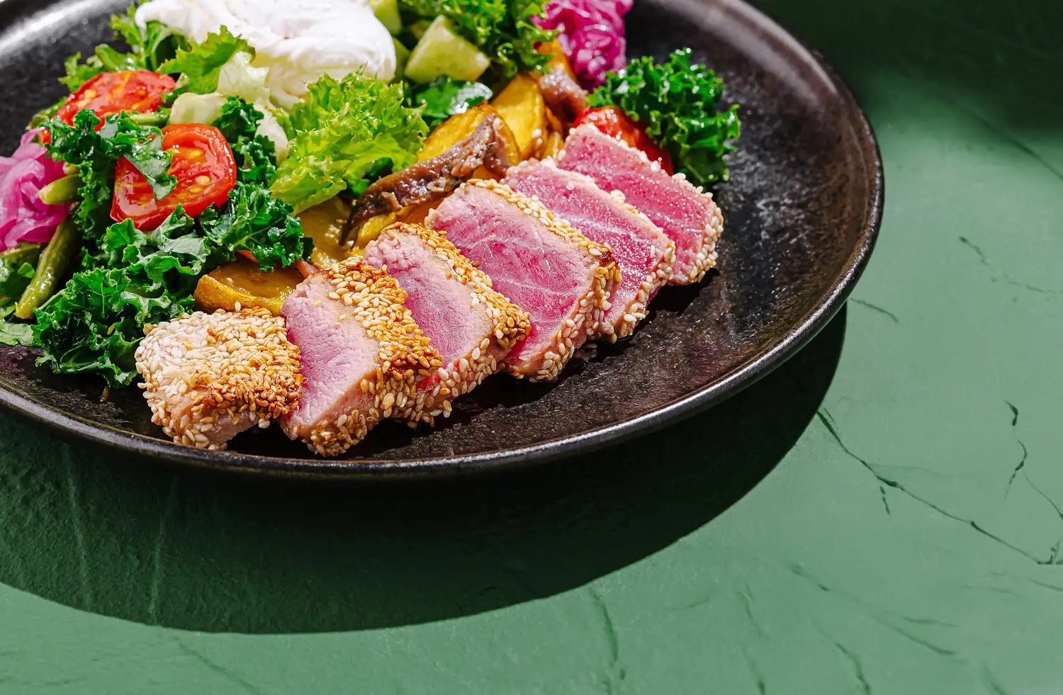 Sliced seared tuna with sesame crust over mixed greens and pickled vegetables.